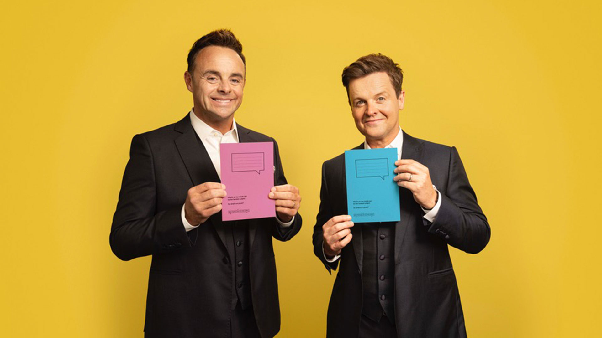 Ant and Dec are standing side by side against a bright yellow background. They are holding pink and blue school jotters. On the front page, there is an image of a speech bubble with lines.